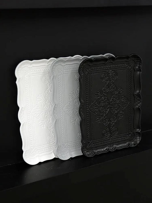 Three decorative embossed trays in black and white with intricate floral and rope patterns on a black surface