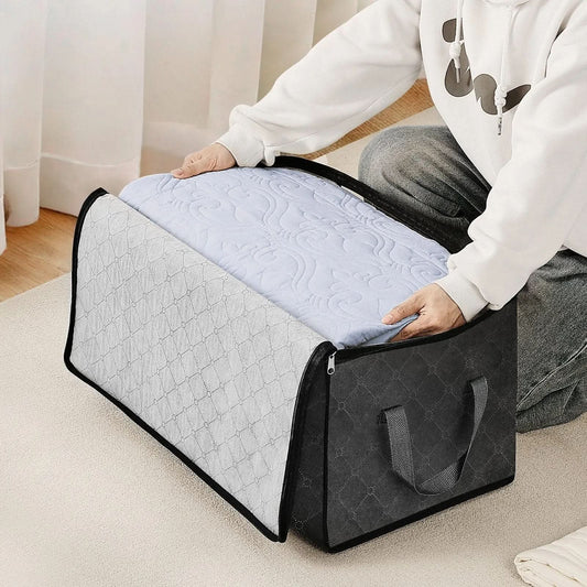 Person placing quilted bedding inside large gray fabric storage bag with handles on carpet