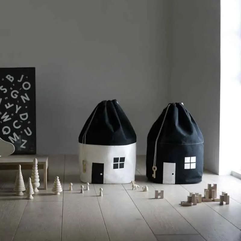 Black and white cotton canvas baby toy storage bags shaped like houses with wooden toys on the floor