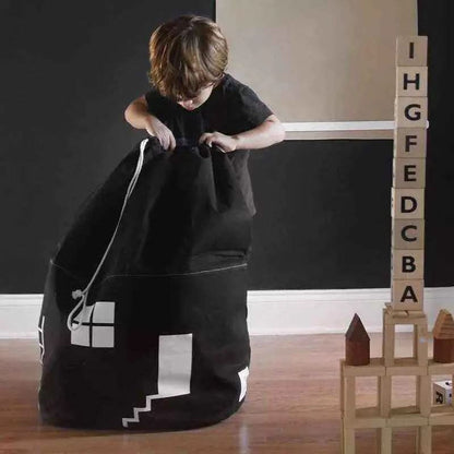 Child playing with large black cotton storage bag shaped like a house in a room with wooden floor and alphabet blocks