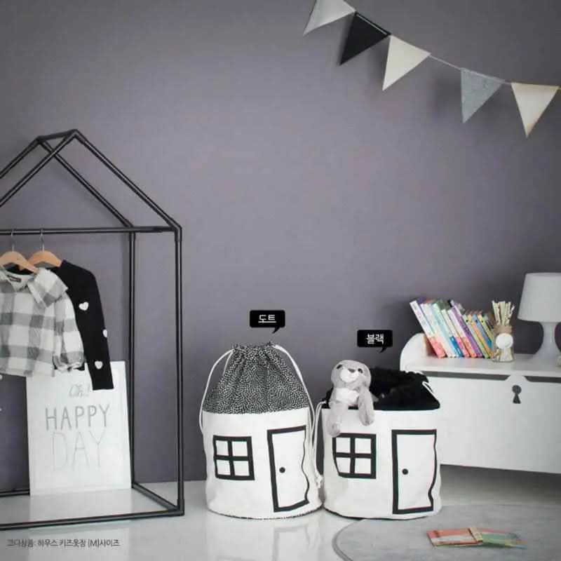 children's room with black and white house-design toy storage bags, plaid shirt on metal frame, and books on white dresser