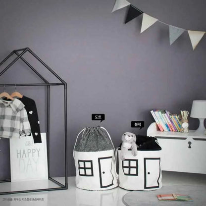 children's room with black and white house-design toy storage bags, plaid shirt on metal frame, and books on white dresser