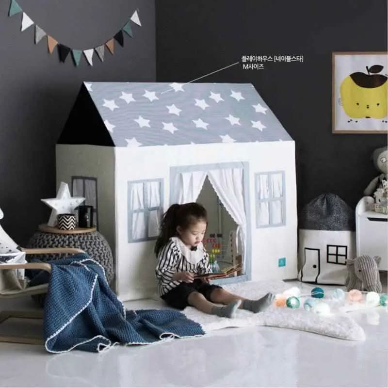 Child reading inside a cotton canvas playhouse with star roof, in a cozy kids room with toys and decor