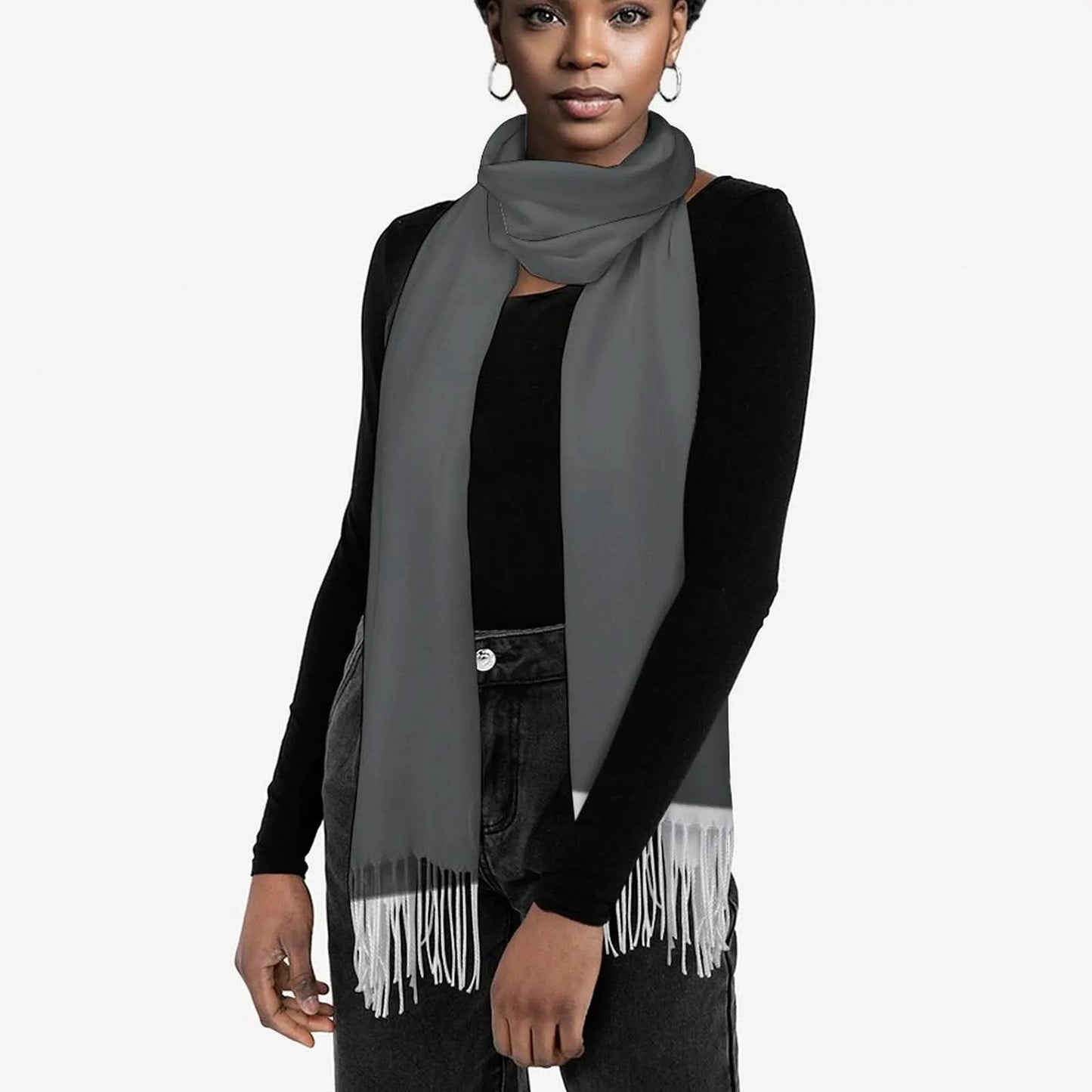 Woman wearing a gray tassel scarf over a black long-sleeve top and dark jeans on white background