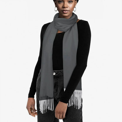 Woman wearing a gray tassel scarf over a black long-sleeve top and dark jeans on white background
