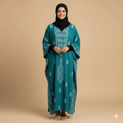 Smiling woman wearing teal V-neck kaftan dress with white floral patterns and a black hijab on beige background