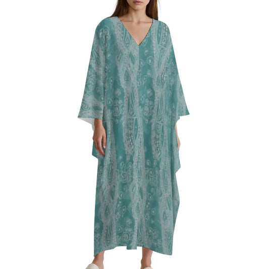 woman wearing teal patterned V-neck kaftan dress with wide sleeves and white shoes on white background